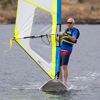 man on a windsurfer at shoreline lake A man windsurfing with his hand extended out on shoreline lake.