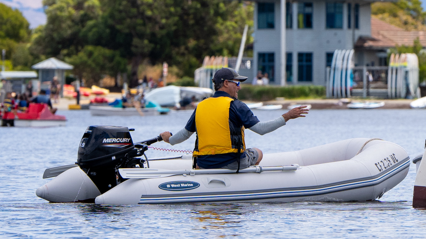 A sailing instructor coaching a sailboat from a powerboat.