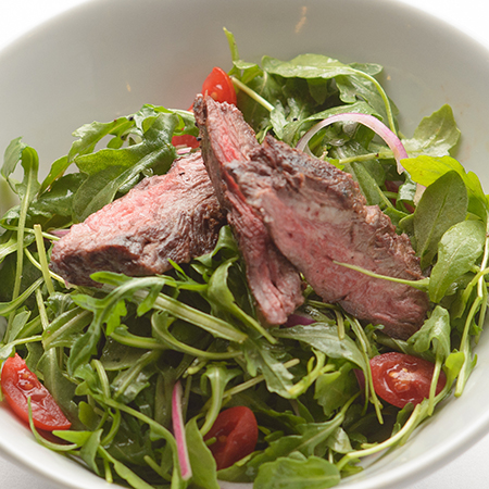 A garden greens salad that is topped with several slices of steak.
