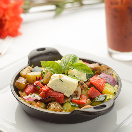 A skillet filled with veggies, potatos and toppped with cheese.