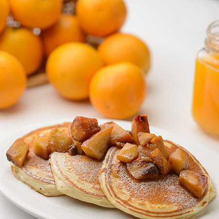 A stack of panckakes with powdered sugar and apples on top.
